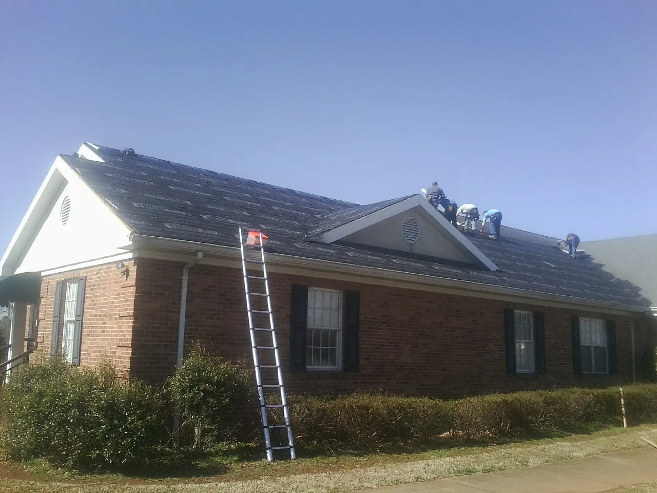 Crew tearing shingles off a brick ranch roof with a ladder set — Emergency Roof Repair work by our crew in Loveland